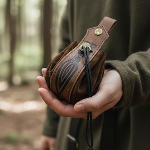 Può includere: Una borsa in pelle marrone caratterizzata da un pannello superiore strutturato con un design geometrico scuro in rilievo, un bottone a pressione in metallo color ottone e una coulisse nera con chiusura in metallo abbinata per il contenuto.