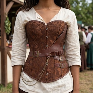 May include: A brown corset featuring a dark brown floral damask pattern, layered with a smooth brown faux leather overlay. The garment includes a front metal busk closure, two side buckles, a horizontal strap with a buckle, and a gold chain detail.