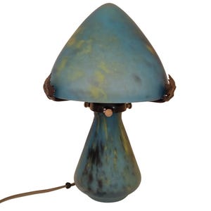 Peut inclure: Lampe de table en forme de champignon avec un abat-jour en verre bleu et jaune. La lampe a une base sombre et un cordon marron. L'abat-jour est de forme conique et la base en forme de goutte d'eau. Luminaire décoratif.