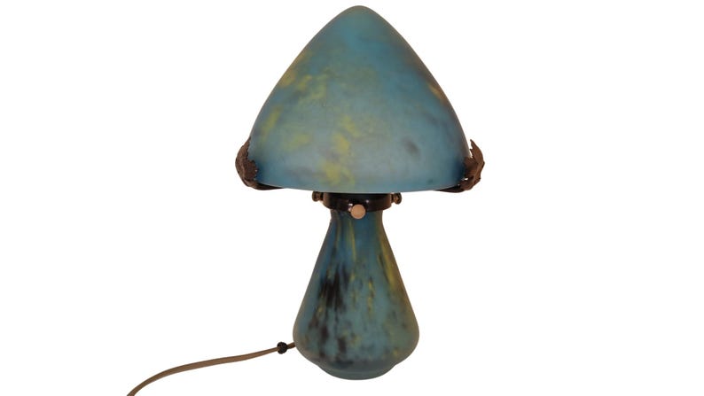 May include: A mushroom-shaped table lamp with a blue and yellow glass shade. The lamp has a dark base and a brown cord. The shade is a conical shape, and the base is a teardrop shape. The lamp is a decorative lighting fixture.