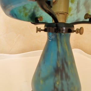 May include: A vintage-style table lamp with a blue and yellow glass shade and base. The lamp features a decorative leaf design on top. The base has a teardrop shape. The lamp has a brass-colored stem and hardware.