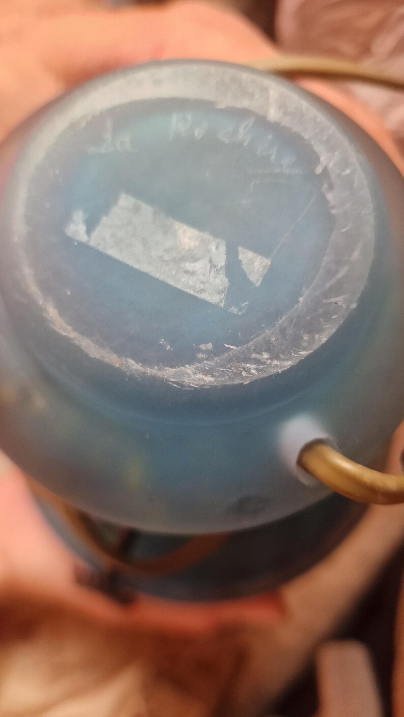 May include: A close-up of the bottom of a light blue glass object. The object has a rounded shape and a frosted appearance. The text "La Roche" is visible on the bottom of the object.