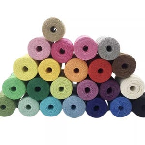 May include: A pyramid of colorful twine spools in various shades, including pink, yellow, green, blue, and brown. The spools are tightly wound and have a central hole. The twine appears to be made of natural fibers, suitable for crafts and packaging.