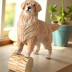 May include: A wooden sculpture of a Golden Retriever dog standing on a log. The dog is carved with detailed texture, showcasing its fur and features. The sculpture is light brown with a natural wood grain finish, perfect for home decor.