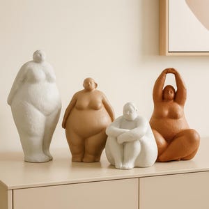 May include: Four ceramic sculptures of stylized human figures in various poses. The figures are in shades of white, tan, and brown. One figure is standing, one is seated with arms crossed, and another is seated with arms raised. The sculptures are on a light-colored surface.