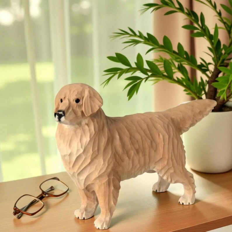 May include: A wooden sculpture of a Golden Retriever dog with detailed carved fur texture. The dog is light brown with a black nose and is standing on a wooden surface. A pair of eyeglasses rests nearby. A potted plant is in the background.