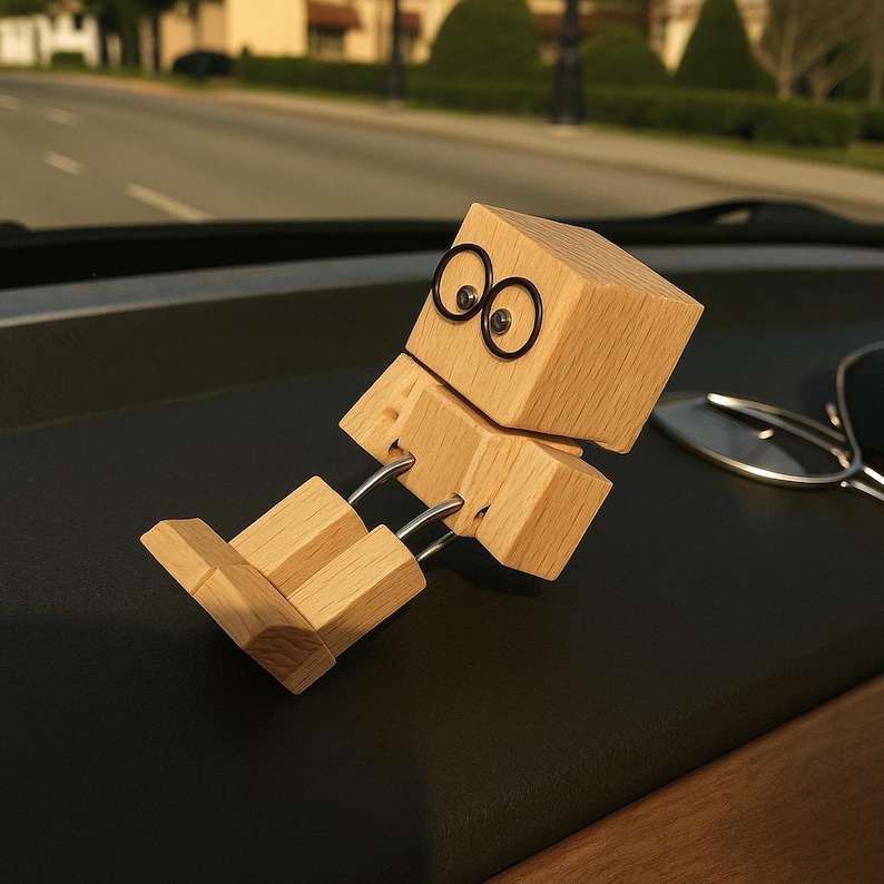 May include: A wooden articulated figure with a block-shaped head and body, connected by metal rods. The figure has black circular eyes and is posed in a reclining position. The figure is made of light-colored wood.