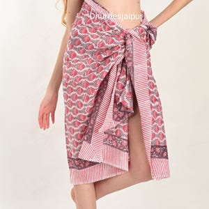 May include: A pink and white sarong with a floral pattern and striped border. The sarong is tied at the waist and falls to the mid-calf. The fabric has a soft, flowing appearance.