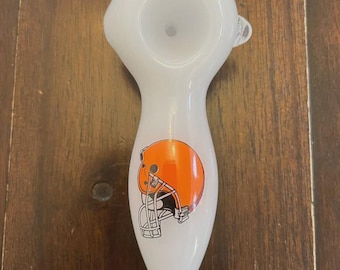 May include: White glass pipe with an orange and brown football helmet graphic. The pipe has a rounded bowl and a long, tapered stem. The helmet graphic is on the stem of the pipe.