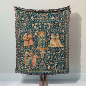 May include: A woven throw blanket featuring a dark teal background with a repeating floral pattern. The central design depicts a cat wearing a crown and robe seated on a throne, surrounded by other cats in medieval attire playing instruments.