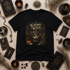 Kitchen Witch shirt featuring a vintage cottagecore folk magic design with herbal cauldron, mystical herbs, stars, and botanical details. Witchy unisex tee inspired by kitchen witchcraft, pagan spirituality, herbalism, and cozy mystical aesthetics. Perfect gift for witches, herbalists, cottagecore lovers, Wiccan fashion fans, and botanical magic enthusiasts.