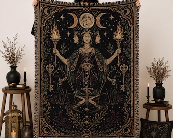 Puede incluir: Una manta tejida con un diseño oscuro e intrincado de una figura de tres caras que sostiene antorchas, flanqueada por dos perros y llaves. La obra incluye motivos celestiales como lunas y estrellas, con un borde decorativo y flecos.