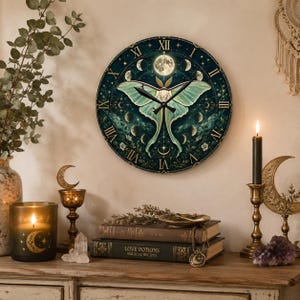 May include: A round wall clock featuring a large pale green luna moth at its center, surrounded by a dark teal background with gold Roman numerals, various moon phases, and small stars. The clock has black hour and minute hands.