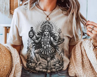 Könnte beinhalten: Beiges T-Shirt mit einer detaillierten Schwarz-Weiß-Illustration einer vielarmigen Gottheit. Die Grafik zeigt Schädel, Flammen und eine Figur, die auf einer Person steht. Das Shirt hat kurze Ärmel und einen Rundhalsausschnitt.