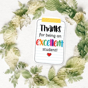 K&ouml;nnte beinhalten: Ein wei&szlig;er Notizblock-f&ouml;rmiger Aufkleber mit dem Text "Thanks for being an excellent student!" in Schwarz und bunten Buchstaben. Unten befindet sich ein rotes Herz. Der Aufkleber ist von einem Kranz aus gr&uuml;nen und hellgr&uuml;nen Bl&auml;ttern umgeben.