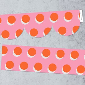 May include: Two pink strips of paper with a repeating pattern of orange circles on a white background. The top strip has a scalloped edge.