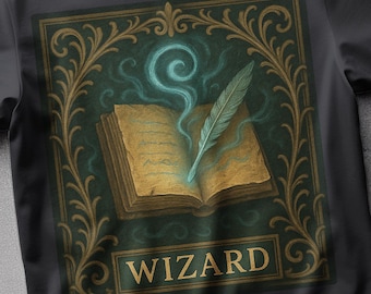 Op de afbeelding: Zwart t-shirt met een illustratie van een open boek, een gloeiende veer en blauwe mist. Het woord "WIZARD" staat in een gouden kader, omringd door gouden en groene versieringen.