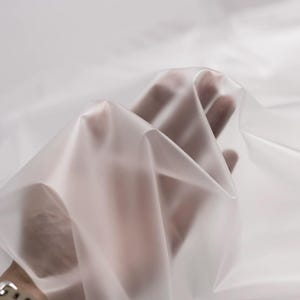 May include: A piece of semi-transparent, frosted white plastic sheeting or fabric. The material is thin and flexible, showing soft folds and creases that create varying levels of opacity and light diffusion across its smooth, matte surface.