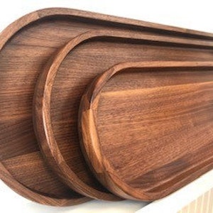 K&ouml;nnte beinhalten: Drei Serviertabletts aus Holz in verschiedenen Gr&ouml;&szlig;en, alle oval geformt mit abgerundeten Kanten. Die Tabletts sind aus dunkelbraunem Walnussholz.