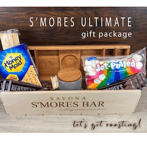 May include: A wooden crate filled with a s'mores gift package. The crate is labeled "Savona S'mores Bar" and "Let's get roasting!" The package includes graham crackers, chocolate bars, marshmallows, and wooden skewers.