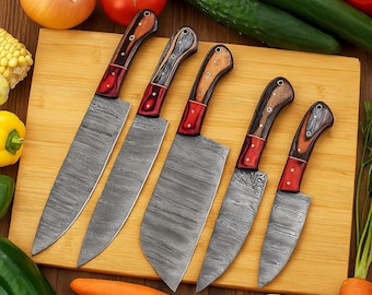 Puede incluir: Un juego de seis cuchillos de cocina con hojas de acero estampadas y mangos de madera. Los mangos presentan una combinación de madera marrón, roja y negra. Los cuchillos están colocados sobre una tabla de cortar de madera.