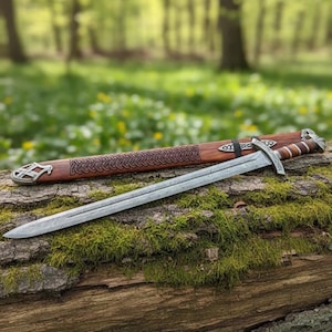 May include: A silver sword with a detailed blade rests on a moss-covered log, next to its wooden sheath. The sheath is brown with a Celtic knot design and metal accents. The background is a blurred forest scene.