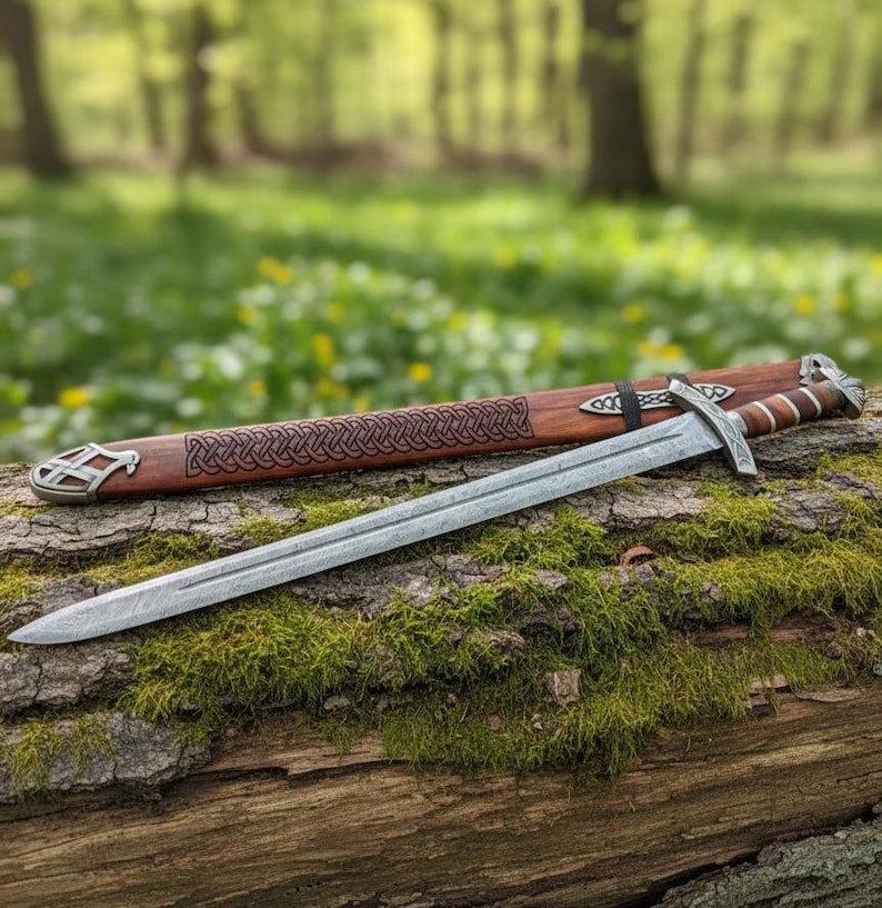 May include: A silver sword with a detailed blade rests on a moss-covered log, next to its wooden sheath. The sheath is brown with a Celtic knot design and metal accents. The background is a blurred forest scene.