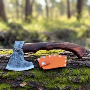 May include: A small hatchet with a dark wooden handle and a silver-colored head. The hatchet rests on a mossy log, accompanied by an orange leather sheath. The handle has a carved design.