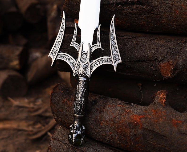 May include: A detailed close-up of a silver sword with an ornate handle and blade. The sword features intricate designs on the hilt and guard, with a polished, reflective blade. The sword is set against a backdrop of dark brown wood.