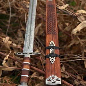 May include: A detailed image of a sword with a patterned blade and a wooden handle with metal accents. The sword is next to its wooden sheath, which has a decorative design and metal fittings. The overall aesthetic is reminiscent of historical weaponry.