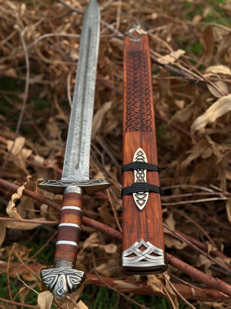 May include: A detailed image of a sword with a patterned blade and a wooden handle with metal accents. The sword is next to its wooden sheath, which has a decorative design and metal fittings. The overall aesthetic is reminiscent of historical weaponry.