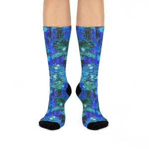 Peut inclure: Une paire de chaussettes montantes arborant un imprimé intégral représentant un étang de nénuphars dans des tons bleu profond, turquoise et vert. Les chaussettes présentent des pointes et des talons noirs unis, contrastant avec le motif artistique.