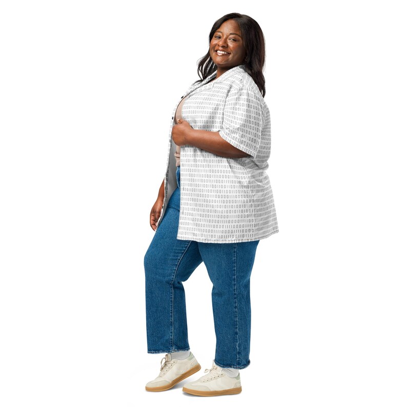 Op de afbeelding: Een overhemd met korte mouwen en knoopsluiting met een verticaal wit en grijs binair codepatroon, gedragen over een effen beige top, gecombineerd met een medium blauwe spijkerbroek en off-white sneakers met lichtbruine zolen op een witte achtergrond.