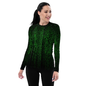 Può includere: Un top a maniche lunghe con un motivo a pioggia digitale nero e verde. Il top è aderente e ha uno scollo tondo. Il design ricorda il codice di un film di fantascienza. La modella indossa leggings neri.