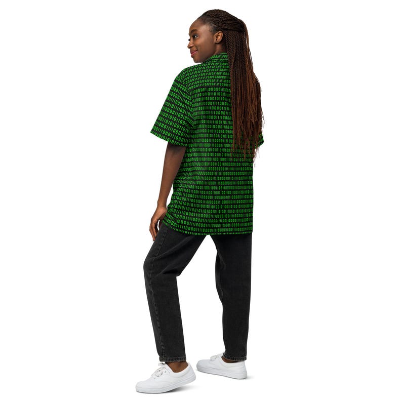 Puede incluir: Una camisa de manga corta con botones y un patr&oacute;n repetitivo de c&oacute;digo binario en negro y verde brillante compuesto por unos y ceros. La camisa se combina con pantalones vaqueros de mezclilla gris oscuro y zapatillas blancas sencillas.