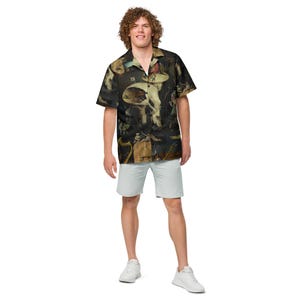 May include: A short-sleeved button-down shirt featuring a dark, detailed painting. The shirt is worn with light blue shorts and white sneakers. The artwork on the shirt has a dark color palette with figures and scenes.