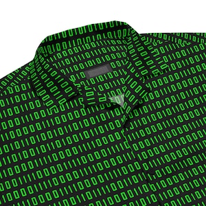 Puede incluir: Una camisa negra de botones con un patr&oacute;n repetitivo de c&oacute;digo binario verde brillante compuesto por unos y ceros. La camisa tiene un cuello est&aacute;ndar, una tapeta de botones frontal y mangas largas, con el patr&oacute;n digital cubriendo toda la tela.