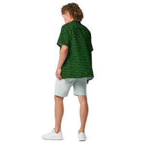 Puede incluir: Una camisa de manga corta con botones, fondo negro y un patr&oacute;n repetitivo de d&iacute;gitos de c&oacute;digo binario en verde brillante. La camisa se combina con pantalones cortos de color gris claro y zapatillas blancas, vista desde una perspectiva trasera.