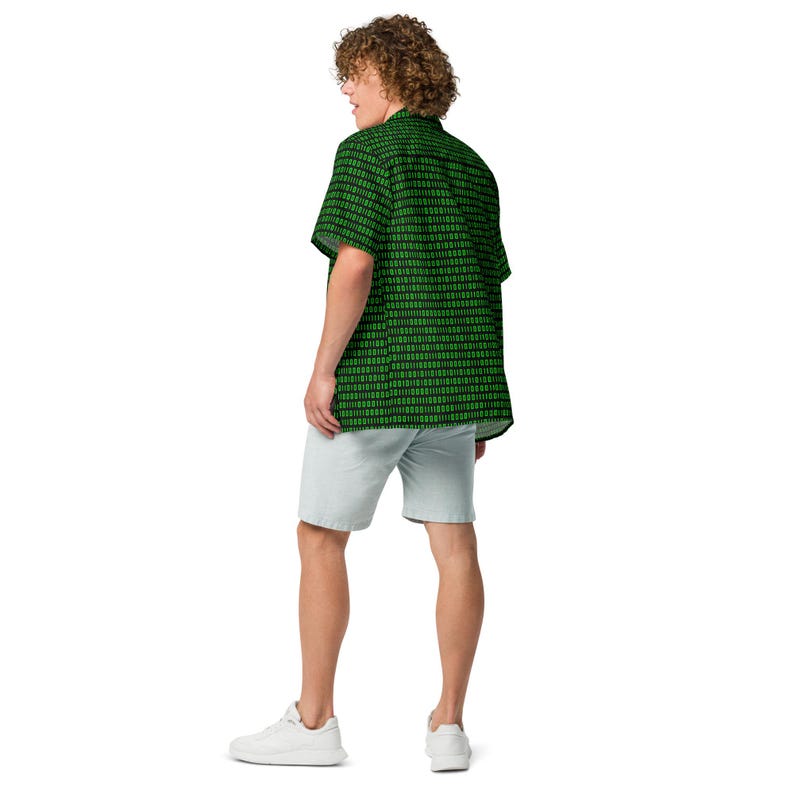Puede incluir: Una camisa de manga corta con botones, fondo negro y un patr&oacute;n repetitivo de d&iacute;gitos de c&oacute;digo binario en verde brillante. La camisa se combina con pantalones cortos de color gris claro y zapatillas blancas, vista desde una perspectiva trasera.
