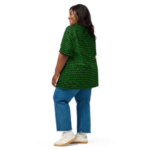 Puede incluir: Una camisa de manga corta con botones, con un fondo negro y un patr&oacute;n repetitivo de d&iacute;gitos de c&oacute;digo binario en color verde brillante. La camisa se combina con pantalones vaqueros azules y zapatillas blancas, creando un conjunto casual y funcional.