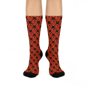 May include: A pair of crew-length socks featuring a repeating pattern of stylised red roses with small green centres set against a solid black background. The socks have a ribbed cuff at the top and a solid black toe and heel section for contrast.