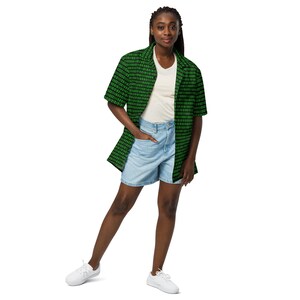 Puede incluir: Una camisa de manga corta con botones y un patr&oacute;n de c&oacute;digo binario en negro y verde, usada sobre una camiseta blanca de cuello en V con pantalones cortos de mezclilla azul claro y zapatillas blancas. La camisa tiene cuello y corte holgado.