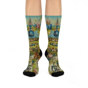 Peut inclure: Une paire de chaussettes montantes arborant une impression détaillée et colorée du Jardin des délices de Jérôme Bosch. Le motif présente des figures complexes, des structures fantastiques et un paysage vibrant dans des tons de vert, bleu et rouge.