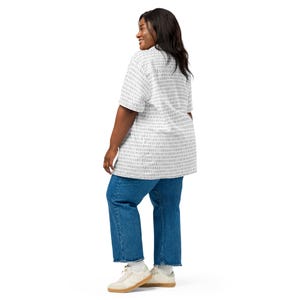 Op de afbeelding: Een overhemd met korte mouwen en een all-over binair codepatroon in grijs en wit, gecombineerd met een blauwe spijkerbroek en witte sneakers. Het overhemd heeft een klassieke kraag en een rechte zoom voor een casual uitstraling.