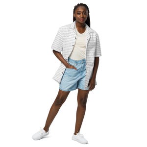 Op de afbeelding: Een overhemd met korte mouwen en knoopsluiting met een wit en grijs binair codepatroon, gedragen over een effen cr&egrave;mekleurig T-shirt met V-hals, lichtblauwe spijkershorts en witte sneakers. Het geheel is casual en heeft een klassieke kraag.
