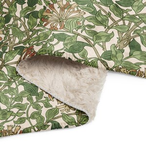 May include: A blanket with a botanical design of green leaves and flowers on a cream background. The blanket has a soft, cream-coloured, plush underside. The design is reminiscent of vintage botanical illustrations. The blanket is ideal for a bed or sofa.