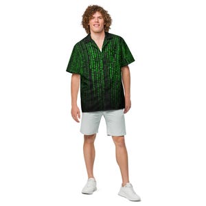 May include: A short-sleeved button-down shirt featuring a black background with a vertical green digital code pattern. The shirt has a notched collar and is paired with light gray shorts and white sneakers, creating a complete casual outfit.