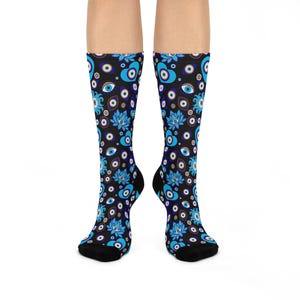 May include: A pair of crew-length socks featuring a black background with a repeating pattern of blue and white evil eye symbols, light blue lotus flowers, and blue heart shapes. The design covers the entire length of the socks up to the calf.