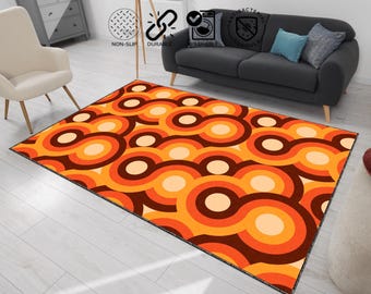 May include: A rectangular area rug with a retro design. The rug features a repeating pattern of interconnected circles in shades of orange, brown, and cream. The rug is placed on a light-colored wooden floor, with a sofa and chair in the background.