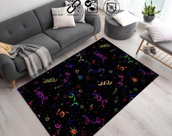 May include: Black rectangular area rug with a colorful confetti pattern. The rug features various shapes like stars, circles, and triangles, along with curly ribbons in multiple colors. The rug is placed in a living room setting.